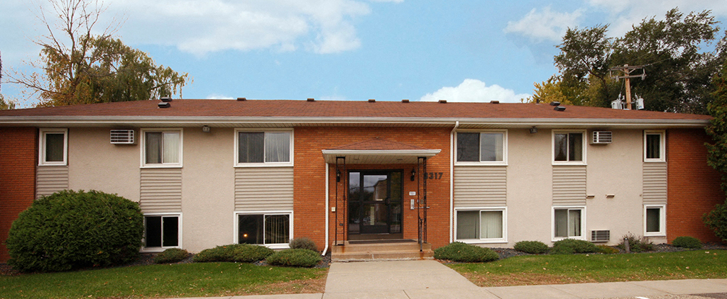 the front of a brick apartment building with a sidewalk